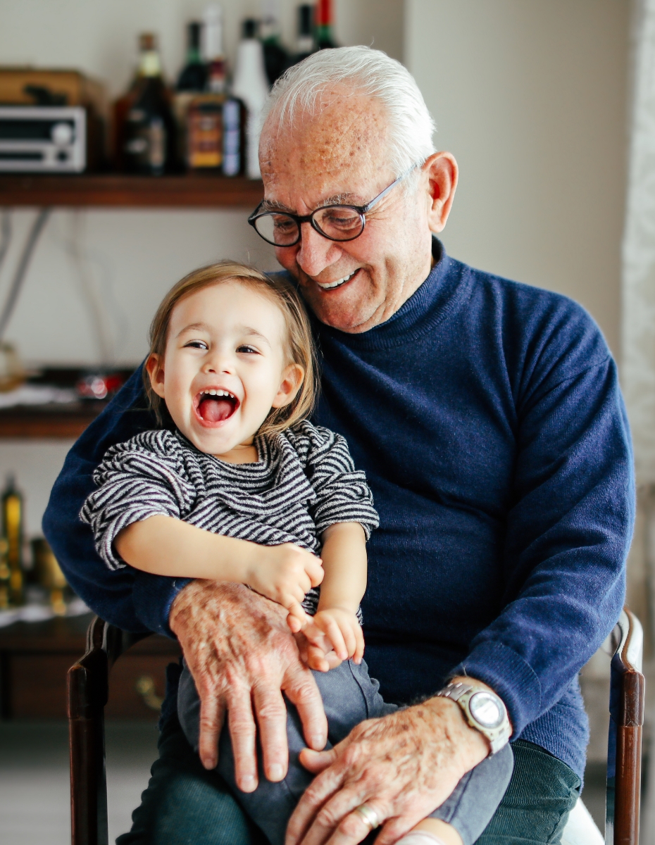 Älterer Mann mit Brille hat kleines Kind auf dem Schoss sitzen. 